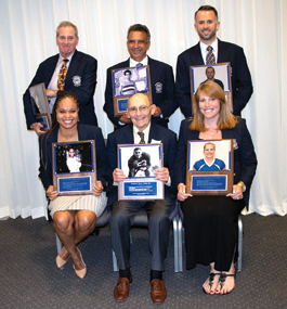 Four men and two women pose with plaques
